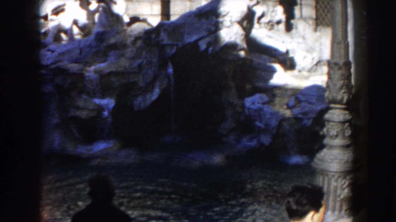 1959 8mm view of Rome's Trevi Fountain with sculpted stone, cascading water, and dark foreground framing.