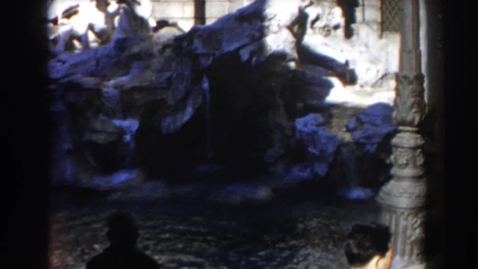 1959 8mm view of Rome's Trevi Fountain with sculpted stone, cascading water, and dark foreground framing.