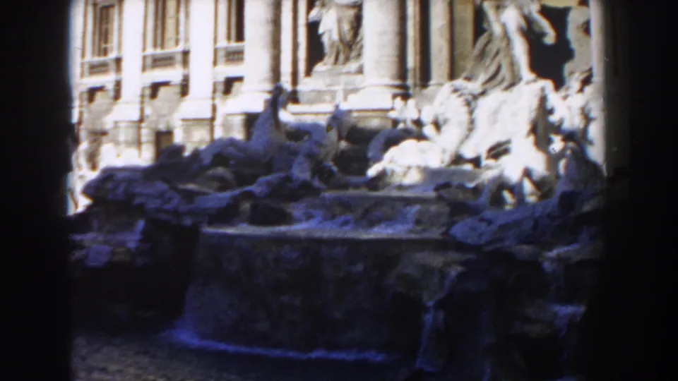 Rome's Trevi Fountain appears in a 1959 8mm frame with sculpted figures, water, facade details, and dark gate-like foreground edges.