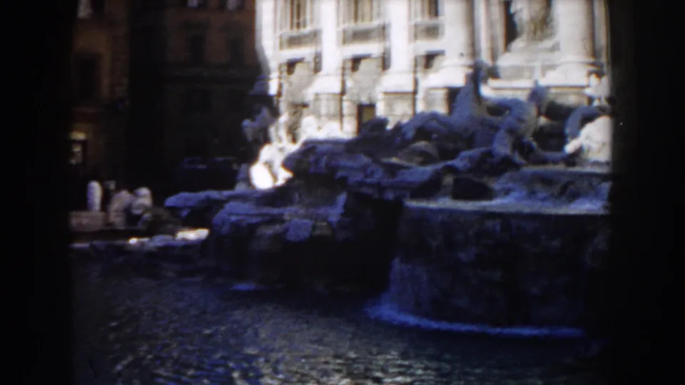 The lower Trevi Fountain basin and rippling water are visible below sunlit columns and shaded sculptural rocks in Rome.