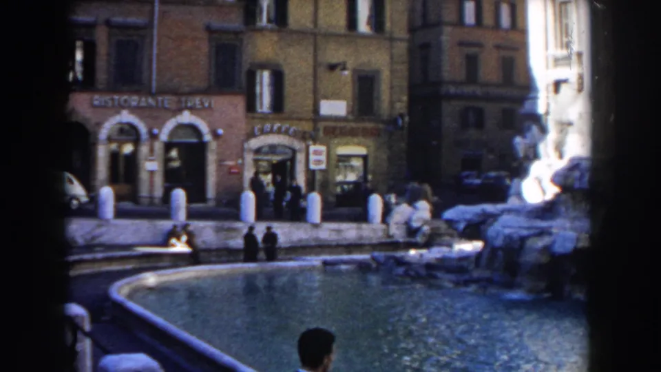 1959 Rome frame with fountain water in the foreground, Ristorante Trevi signage, cafe frontage, pedestrians, bollards, and parked cars.