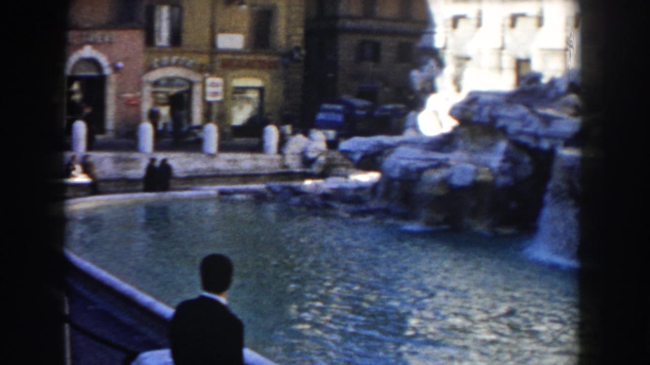 Trevi Fountain basin with pedestrians and buildings beyond the water.