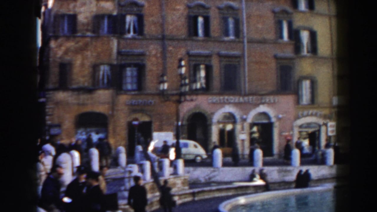 Rome street scene with pedestrians, parked cars, storefronts, and a fountain edge.