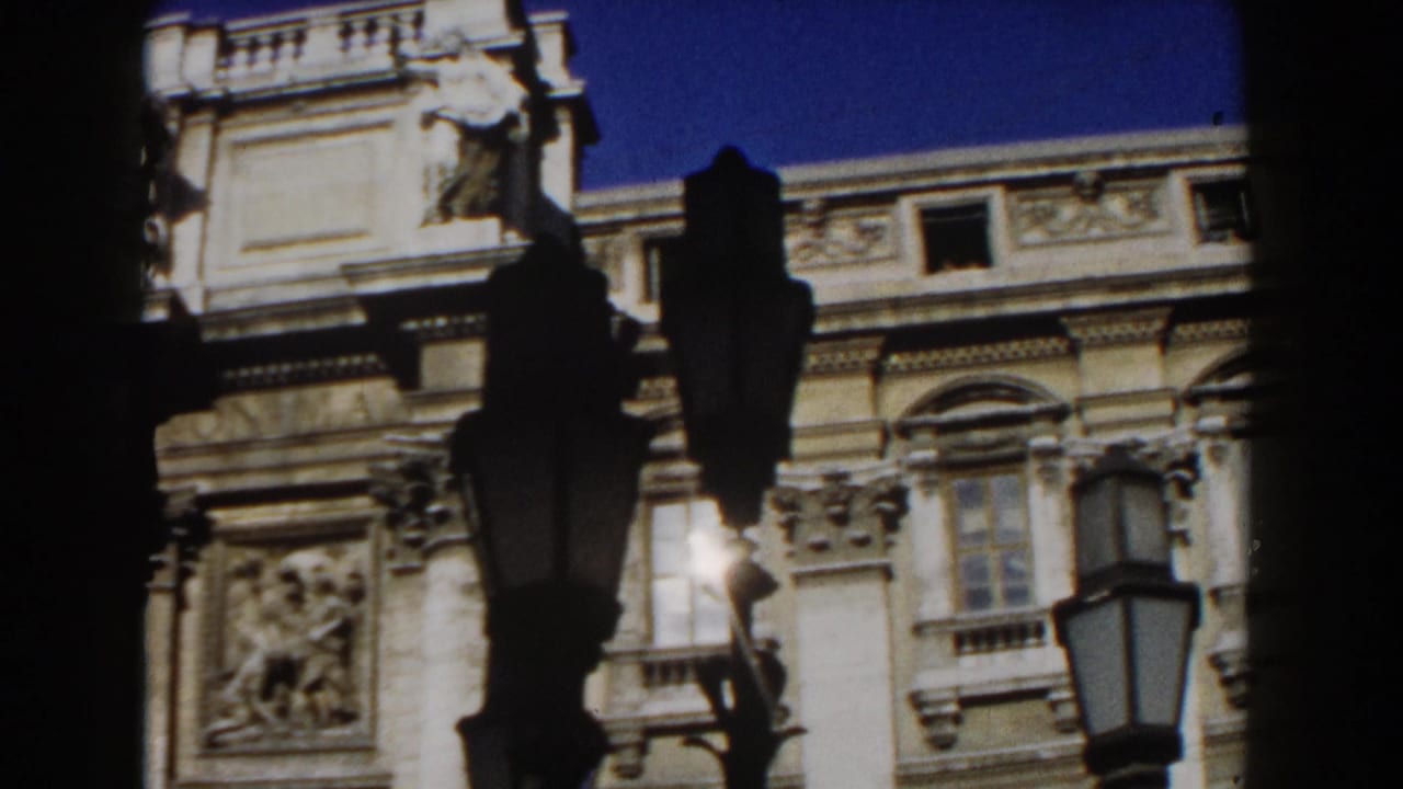 1959 Rome 8mm frame showing part of an ornate historic facade, arched windows, stone carving, and silhouetted lampposts.