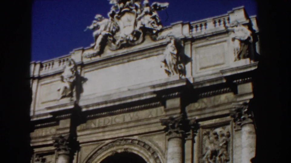 1959 Rome 8mm frame showing an ornate building entrance area with crest, columns, carved panels, and lamppost silhouettes.