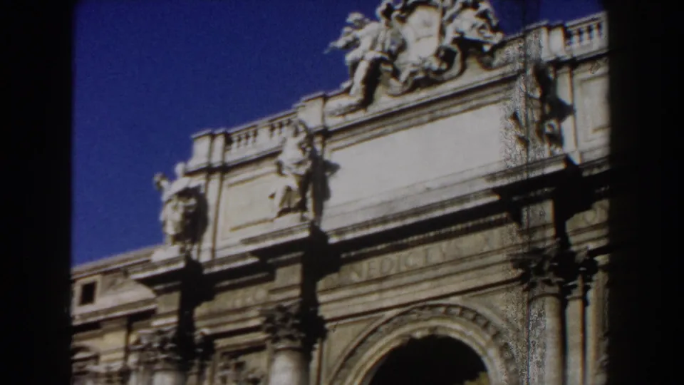 1959 Rome 8mm frame capturing the right side of an ornate historic facade with crest detail, arch, columns, and foreground shadow.