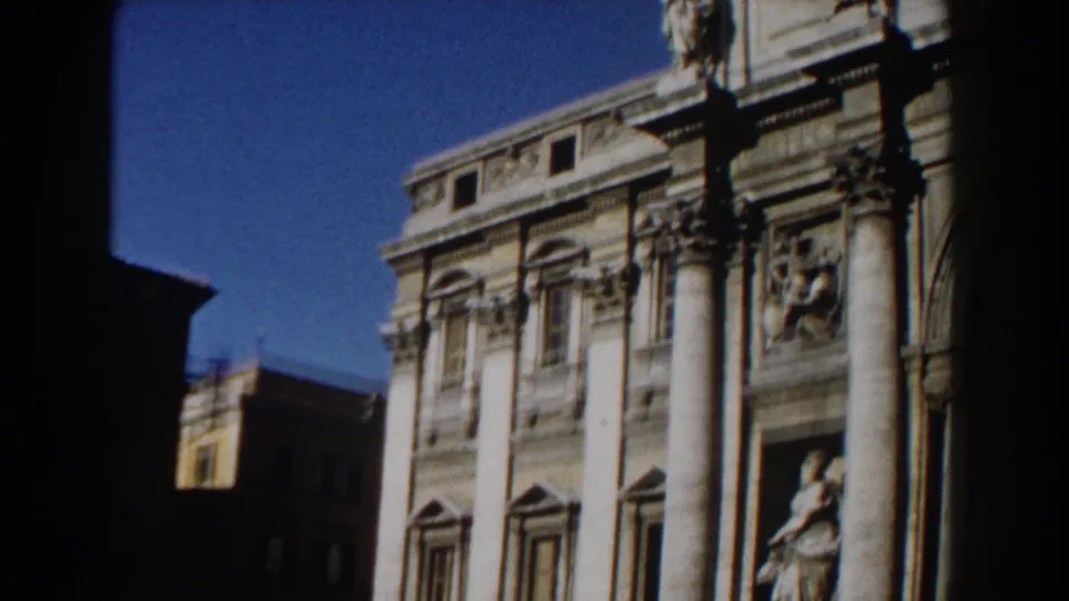 Rome 1959 frame with a pale stone landmark facade, tall columns, sculptural niches, and a dark vertical foreground shadow.