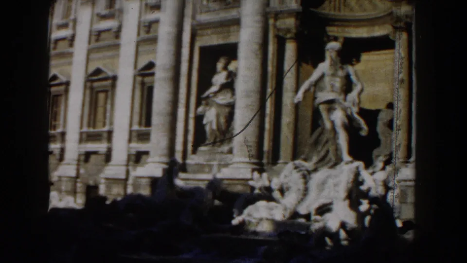 1959 Rome frame showing fountain statuary before a columned public landmark facade with niches, figures, and strong sun-shadow contrast.