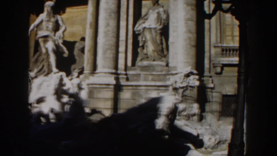 1959 Rome frame showing the Trevi Fountain's central sculpture, columned facade, side statue, and shaded fountain rockwork.