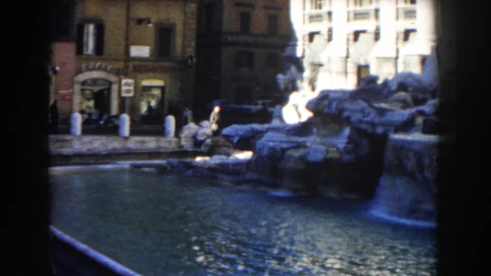 1959 Rome home-movie frame showing Trevi Fountain water, sculpted rockwork, nearby buildings, and dark scan borders.