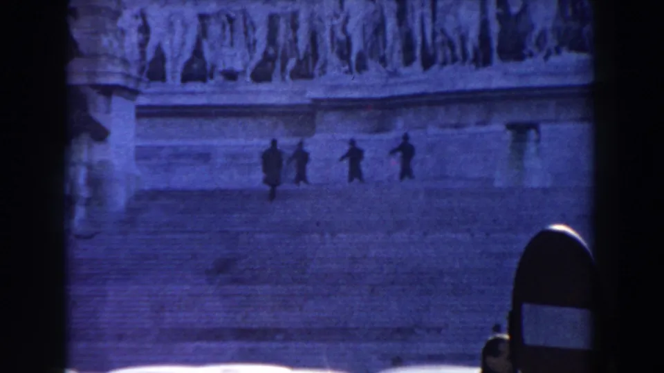 Distant figures move horizontally across Rome stone steps in a blue-tinted 1959 8mm view framed by dark vertical edges.