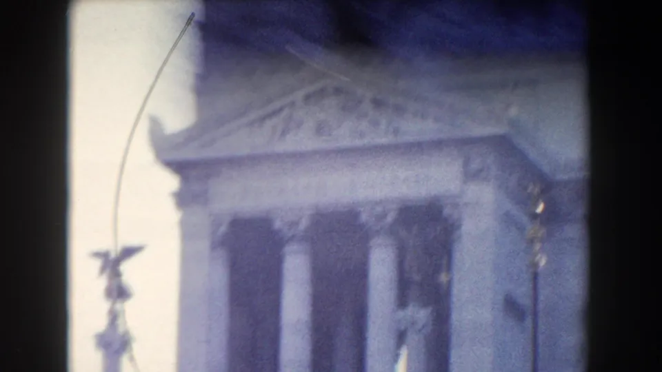 1959 Rome home-movie frame showing columns and a roofline, with a small winged statue silhouetted near the left edge.