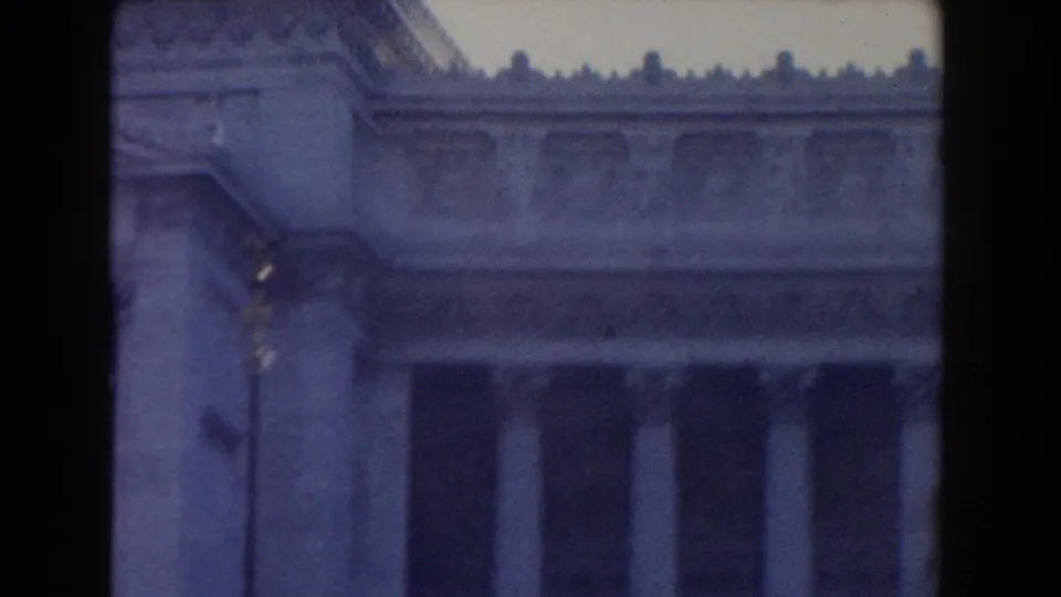 1959 Rome home-movie frame showing a large classical stone facade with tall columns and decorative roof molding.