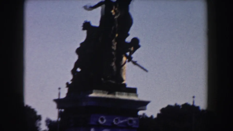 1959 Rome frame showing a dark statue silhouette on a pedestal, with open sky and tree line around the monument.