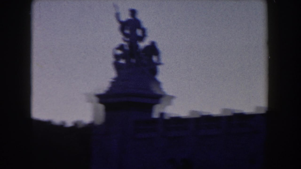 Silhouetted rooftop statue above a dark architectural edge against a pale sky.