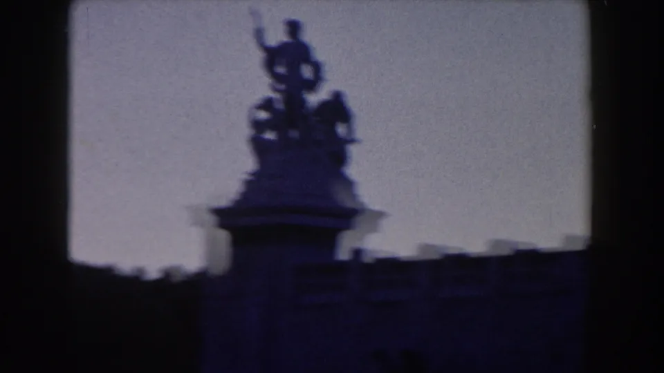 1959 Rome 8mm frame showing a silhouetted statue or sculptural group on a rooftop or monument against a pale sky.