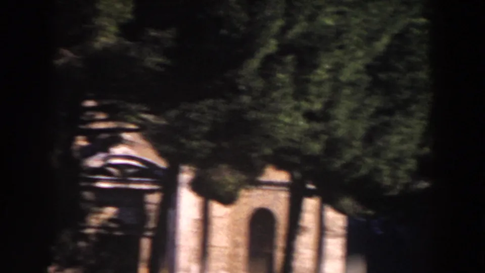 1959 Rome home-movie frame with trees partly obscuring a sunlit stone facade and arched opening.