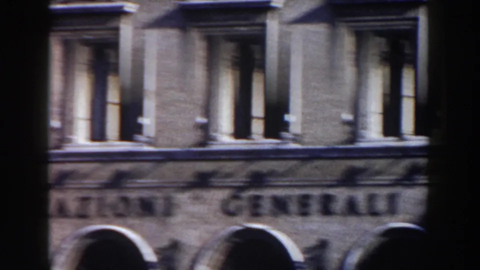 1959 Rome frame showing a building facade with tall windows, arched lower openings, shadows, and indistinct signage.