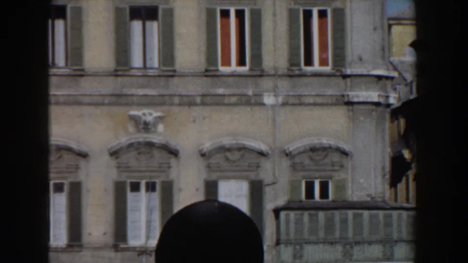 1959 Rome home-movie view of a light stone facade with shuttered windows, cornices, and a dark vertical obstruction in the foreground.