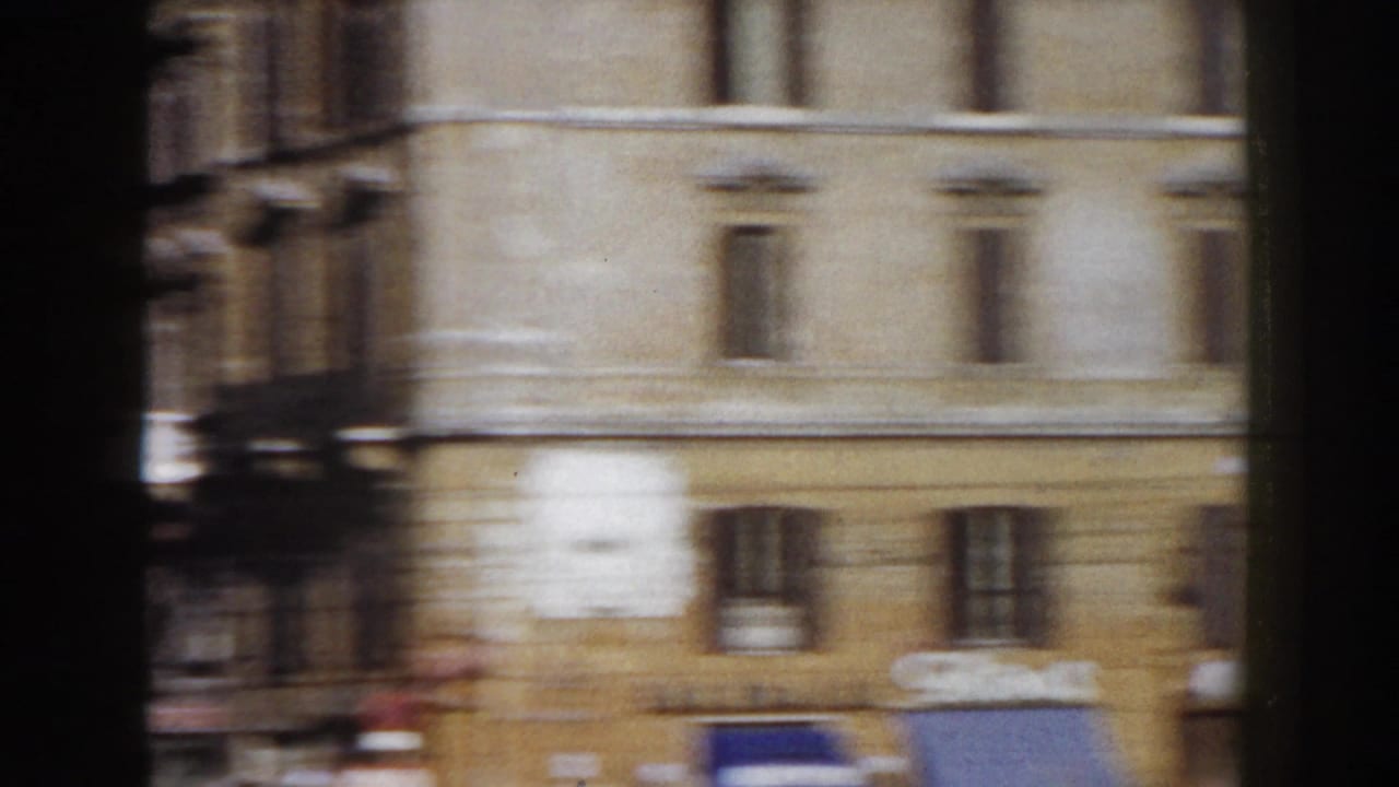 1959 Rome street view from a moving vehicle, with pale masonry facades and dark vertical framing in the foreground.