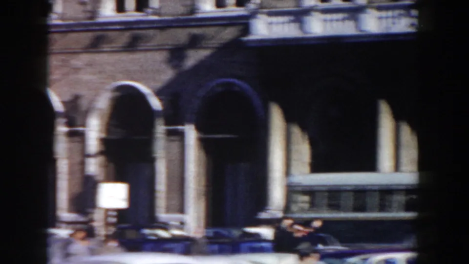1959 Rome view of an arched portico or colonnade, with older cars and pedestrians passing below.