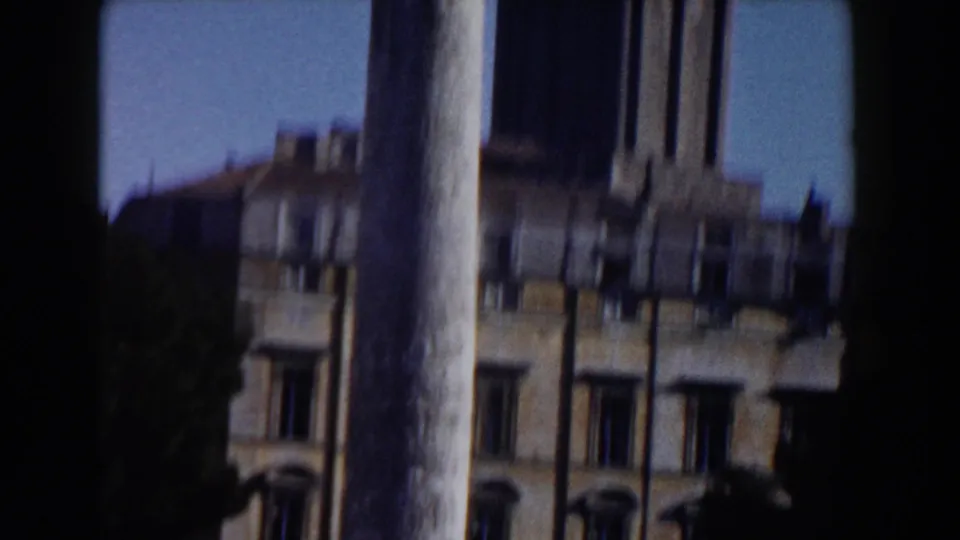 Rome architectural view with a tall column, partial statue top, historic facade, and blue sky in soft 8mm focus.