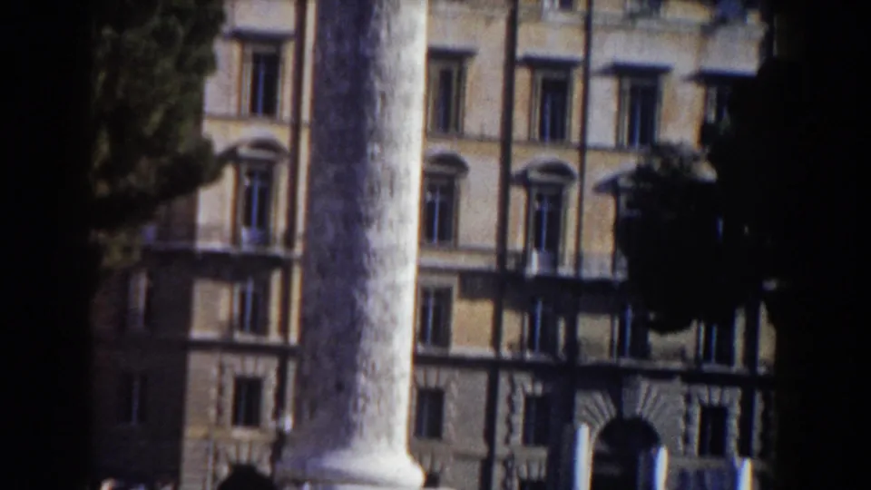 1959 Rome home-movie frame showing a large column, arched windows, and a historic-looking facade in bright daylight.