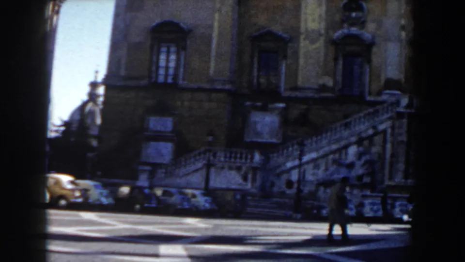 1959 Rome frame showing a grand exterior staircase, weathered facade, parked cars, and a pedestrian crossing the street.
