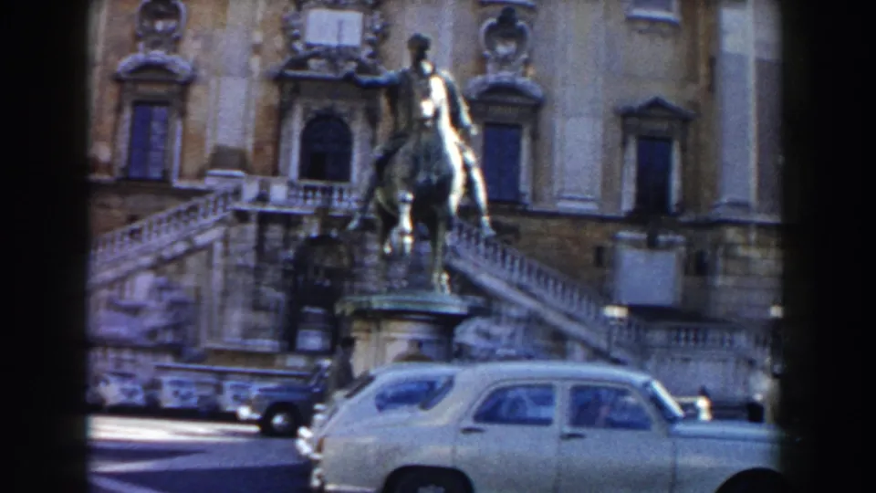 1959 Rome 8mm view of a horse-and-rider statue before a formal stone building, with a pale car crossing the foreground.
