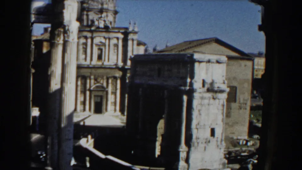 1959 Rome travel frame showing a historic facade, a weathered stone tower, columns, and city buildings under clear sky.
