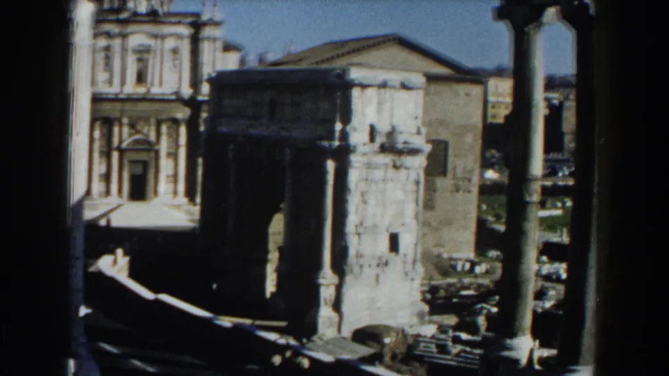 1959 Rome frame with columns and a weathered stone tower in front of historic buildings, ruins, and partial road traffic below.
