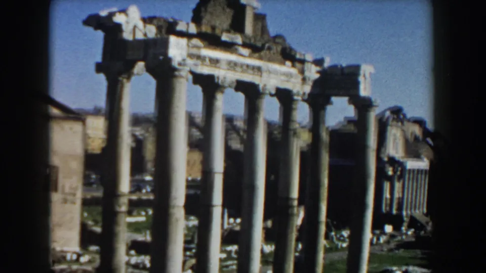1959 Rome 8mm frame showing a row of classical columns, broken entablature, pale ruins, and surrounding urban buildings.