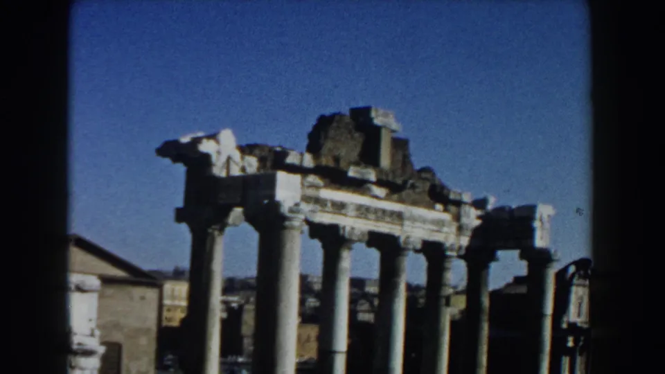 1959 Rome home-movie frame showing tall pale columns and ruined stone structures against a clear blue sky.