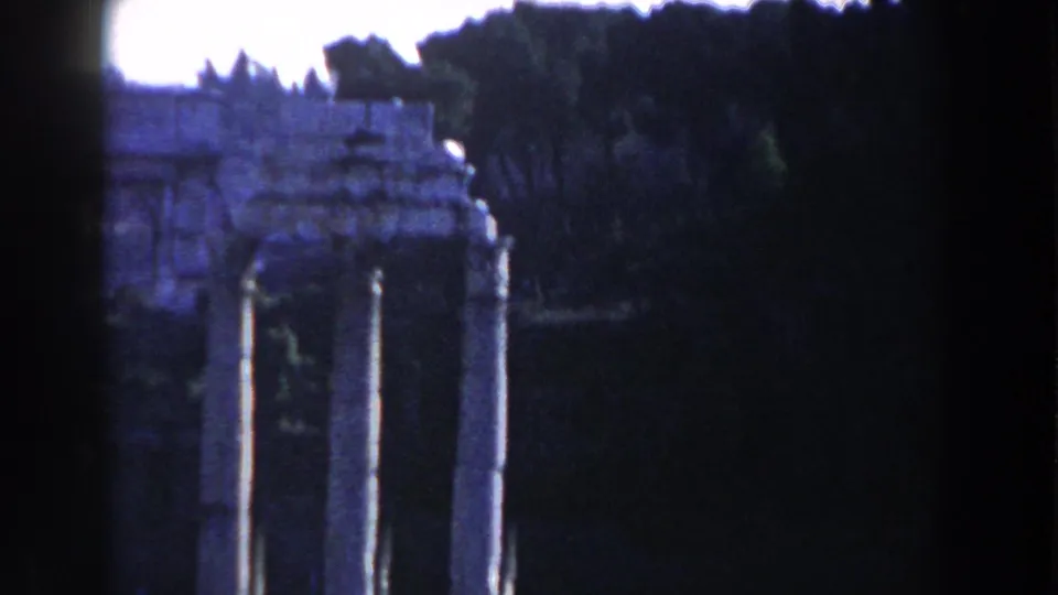 1959 Rome travel frame showing a weathered stone arch with columns, dark trees, and bright sky in soft color 8mm.