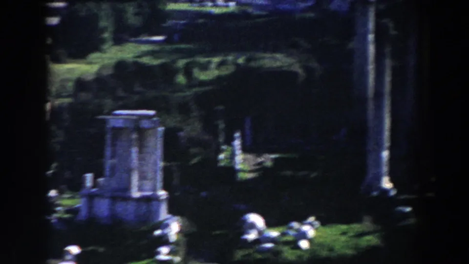 Vintage 8mm Rome frame shows a broken stone feature, upright columns, grass, and fragments across the historic grounds.