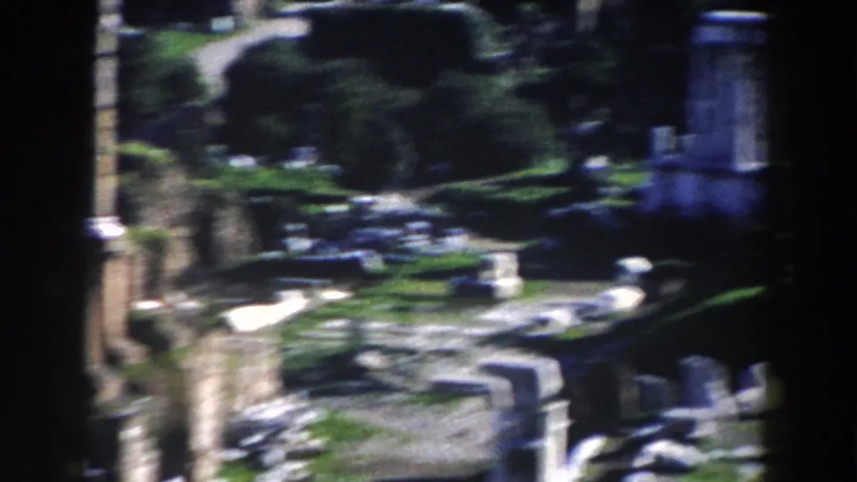 1959 Rome 8mm frame captures stone walls, column remains, shrubs, and scattered masonry during the pan across ruins.