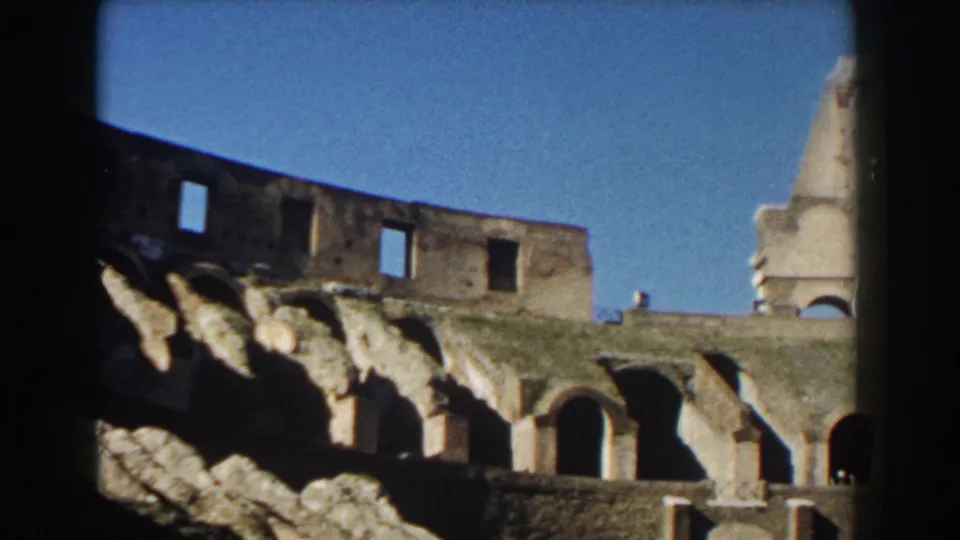 The Colosseum in Rome appears under a blue sky, showing weathered stone walls, arched openings, and sunlit upper ruins.