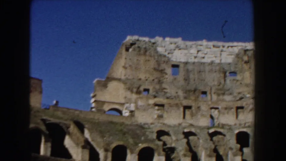 1959 Rome footage showing the Colosseum's upper stone wall, arched gaps, and weathered surface against a deep blue sky.