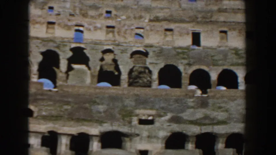 Rome's Colosseum facade appears behind a dark vertical frame edge, with arched bays, small windows, and worn masonry visible.