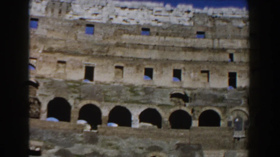 The Colosseum's lower arches and worn stone courses fill the frame, with small distant visitors visible near the lower edge.