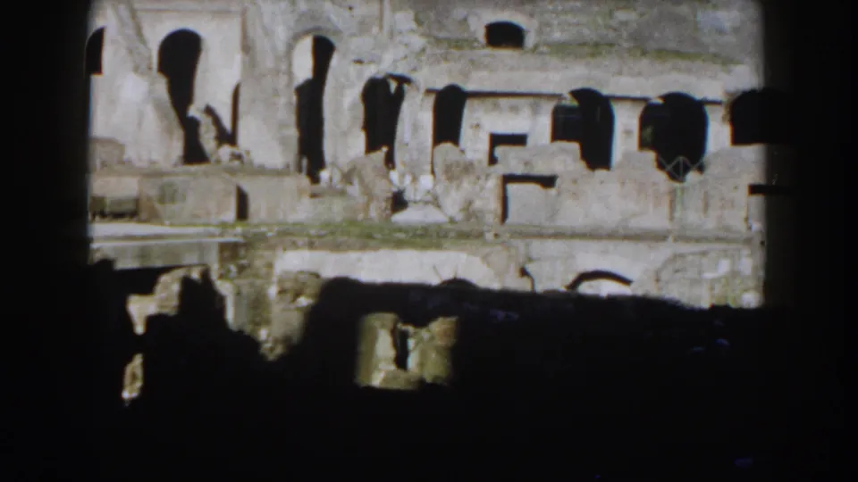1959 8mm frame showing a lower interior section of the Roman Colosseum with tall arched voids, rough stone, and heavy shadowing.