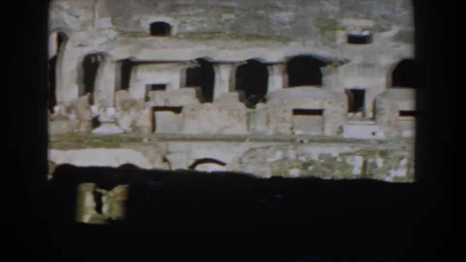 1959 Rome home-movie still of the Colosseum interior, showing rough stone walls, arched recesses, and shadowed architectural remains.