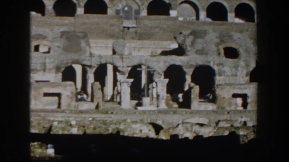 1959 Rome home-movie frame of the Colosseum facade with arches, columns, and shadowed foreground obstruction.
