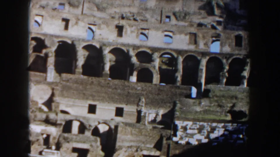1959 8mm frame inside the Colosseum showing lower arches, stone surfaces, and part of the exposed arena structure.
