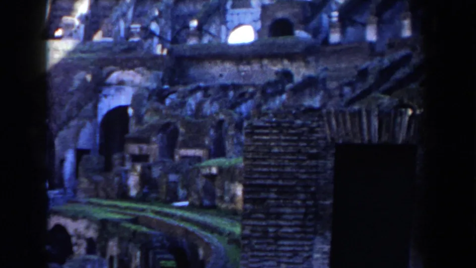 Blue-toned 1959 8mm view of the Colosseum interior, showing shadowed arches, brickwork, and exposed archaeological walkways.
