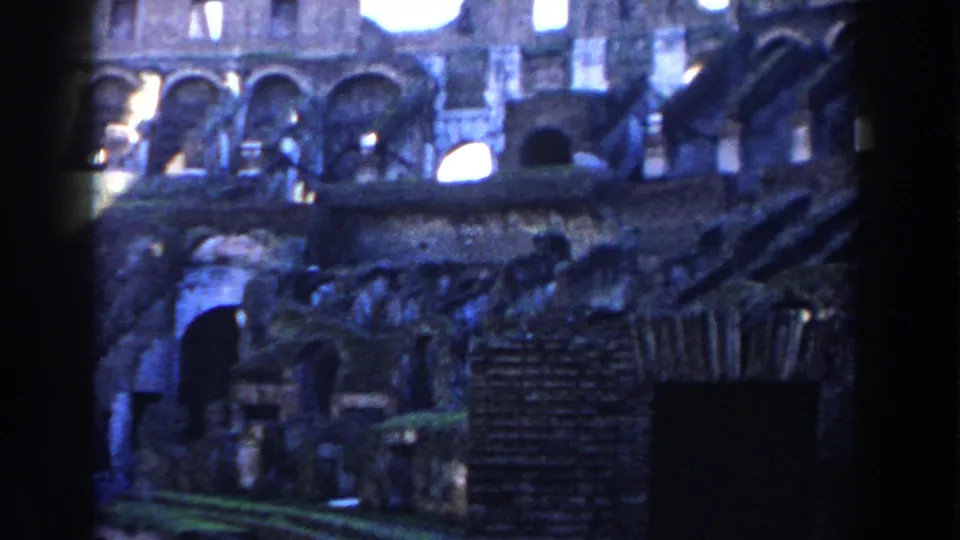 1959 8mm view inside the Roman Colosseum, showing weathered arches, dark openings, and rough stonework.