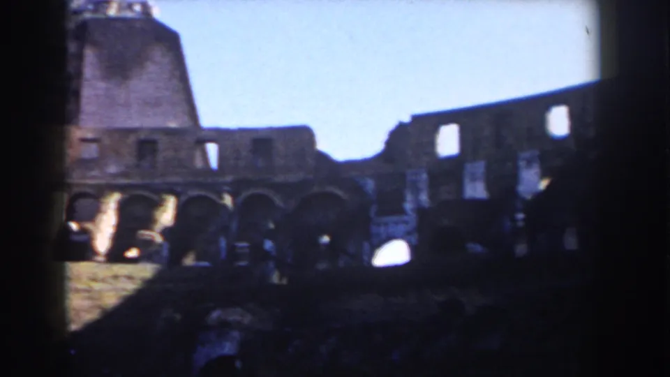 1959 visitor-shot frame of the Roman Colosseum interior, with bright sky above shadowed arches and worn masonry.
