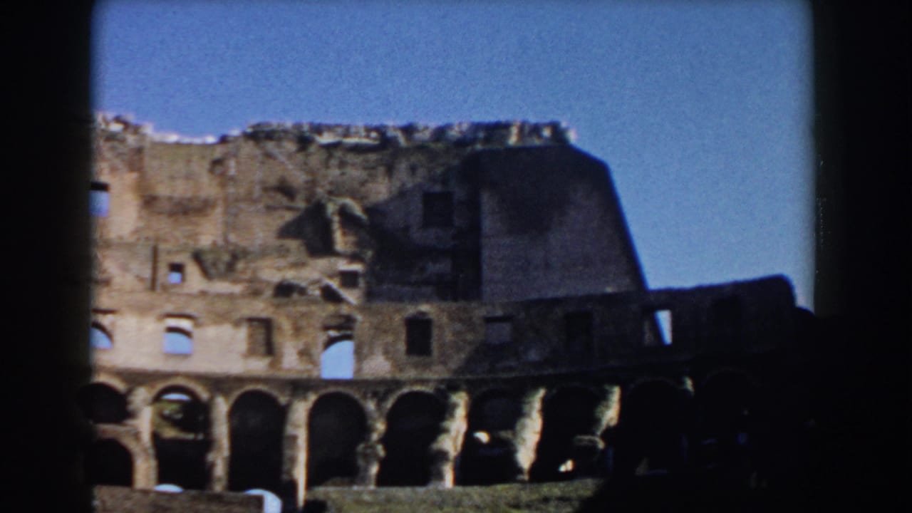 1959 8mm view of the Colosseum in Rome, showing weathered exterior arches and broken upper masonry beneath a clear sky.