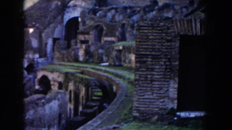 1959 8mm view inside the Colosseum in Rome, with curved ruin passages, brickwork, grassed surfaces, and dark arched openings.