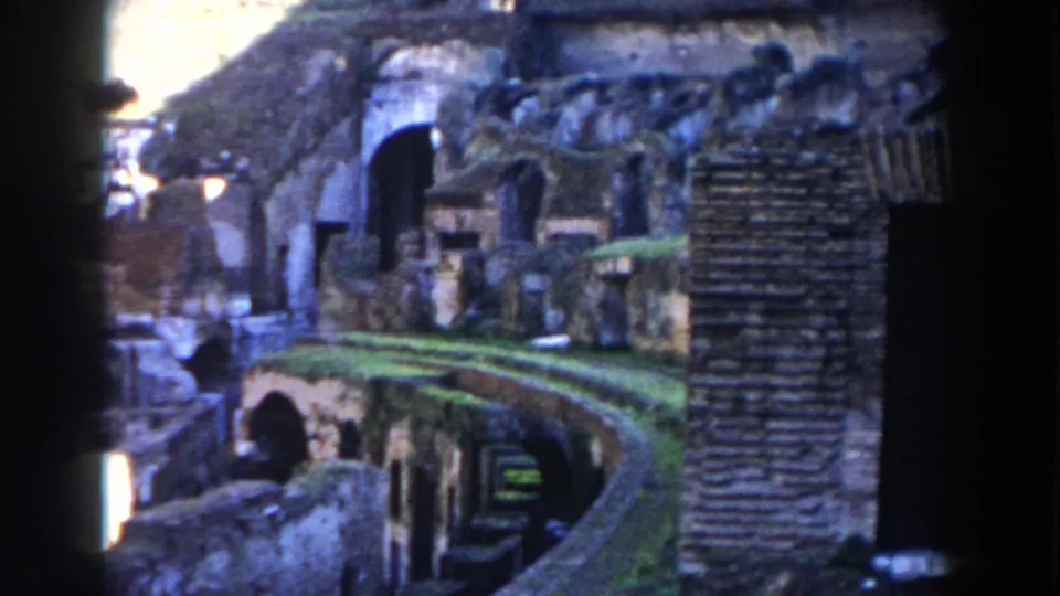 1959 8mm frame from inside the Colosseum, showing layered masonry, a curved passage edge, and weathered arched openings.